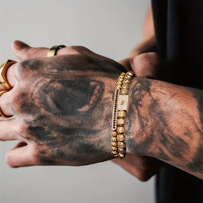 Tattooed arm with gold bracelet and ring on a neutral background