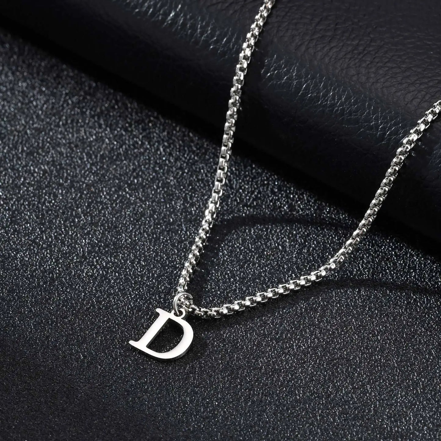 Silver necklace with a 'D' pendant on a black textured background