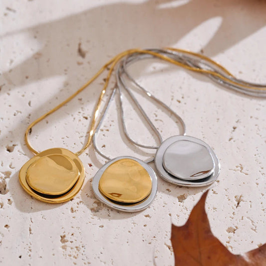 Three necklaces with round pendants in gold, silver on a textured surface.