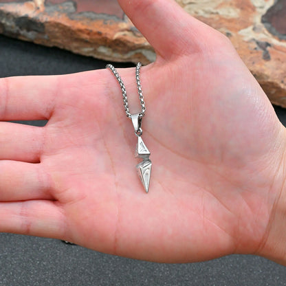 Silver necklace with a pendant held in a hand against a natural stone background
