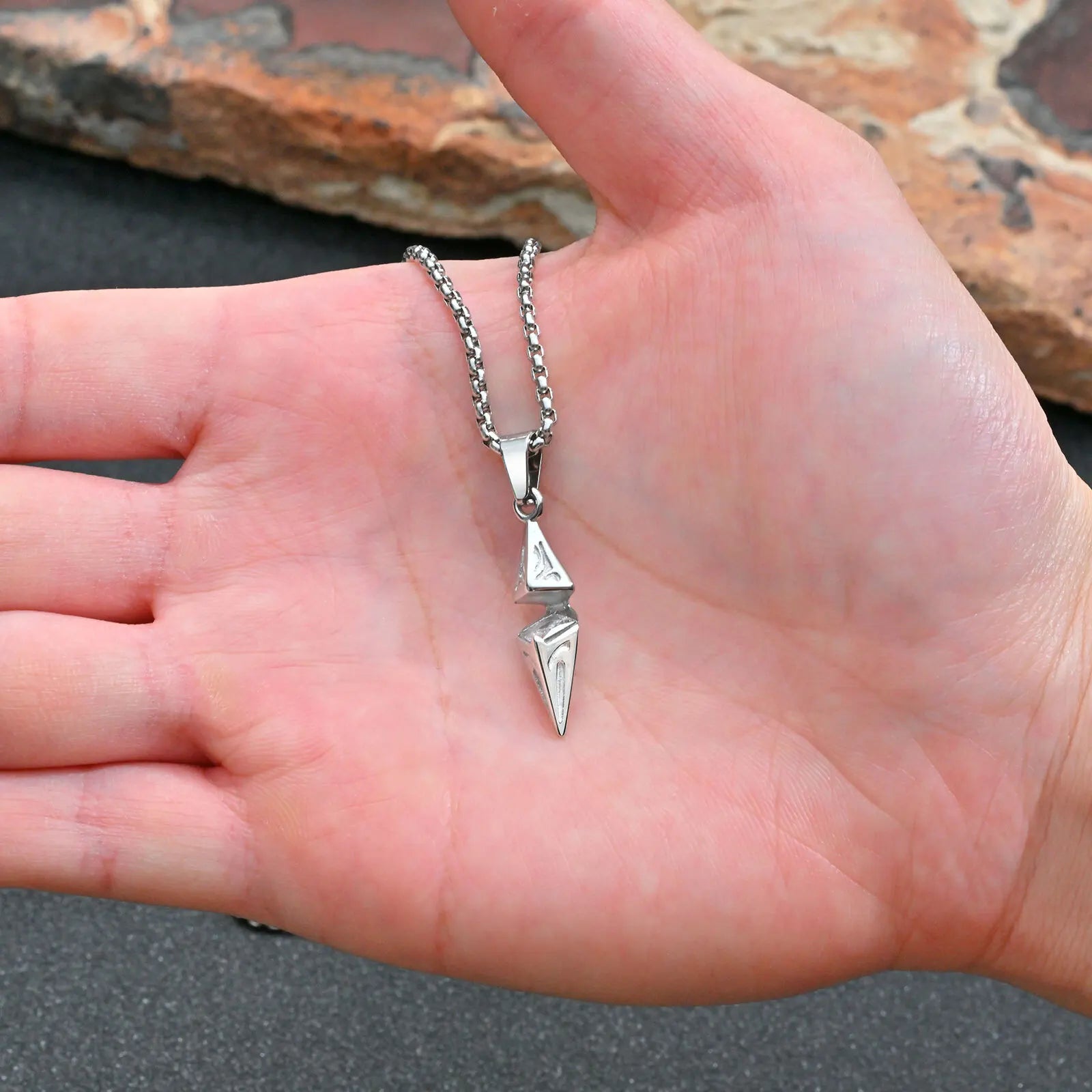 Silver necklace with a pendant held in a hand against a natural background
