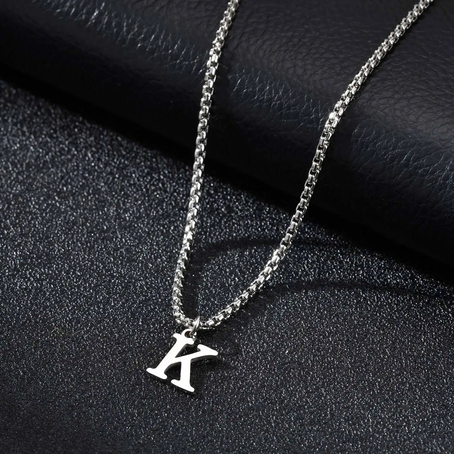 Silver necklace with a 'K' pendant on a dark textured surface