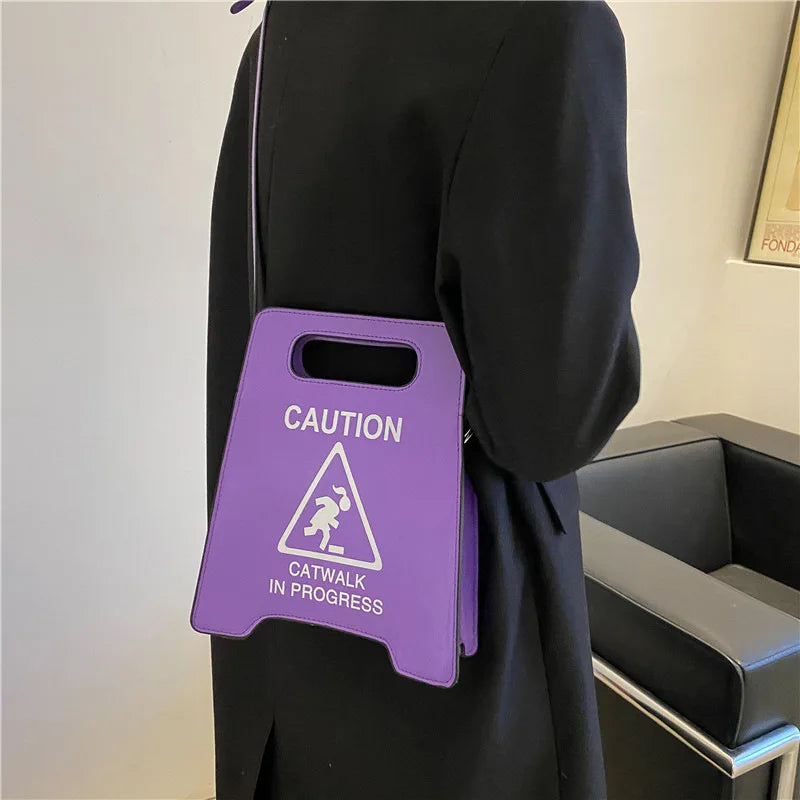 Person holding a purple bag with 'Caution: Catwalk in Progress' text and symbol.