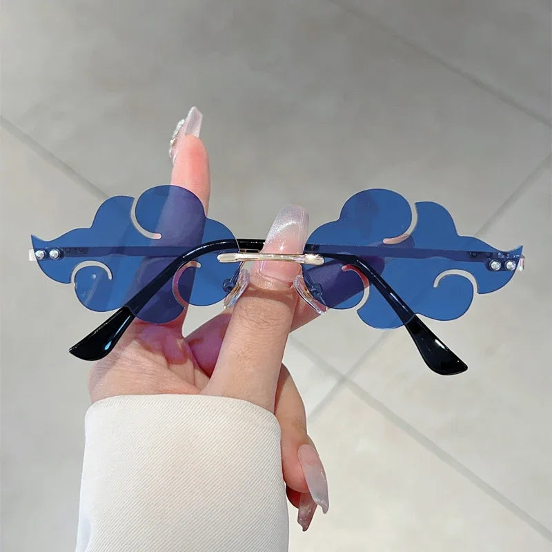 Sunglasses with blue cloud-shaped frames held by a hand against a light background