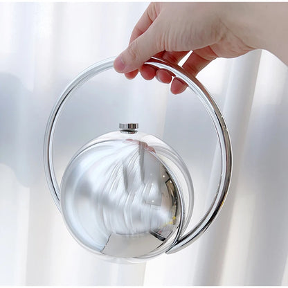 Hand holding a round clutch bag with a reflective surface against a white background