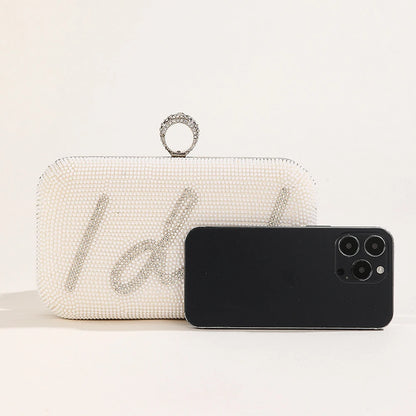 White beaded clutch with 'I do' text and a black phone on a light background