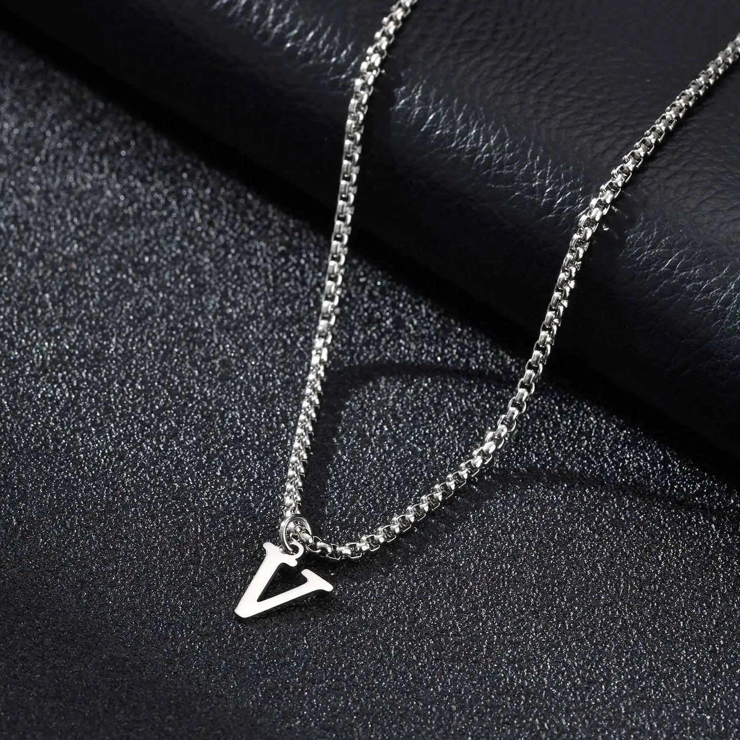 Silver necklace with a letter 'V' pendant on a black textured surface