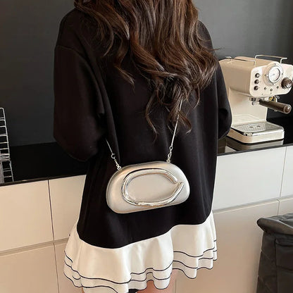 Person wearing a black top and white skirt with a silver handbag in a kitchen setting.