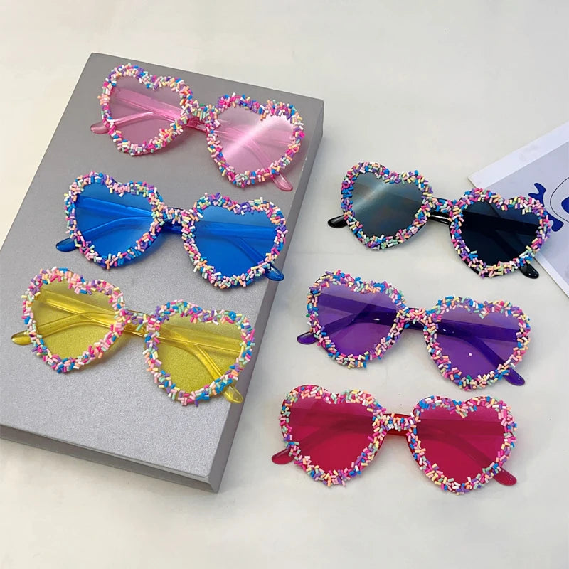 Colourful heart-shaped sunglasses with decorative frames on a grey surface.