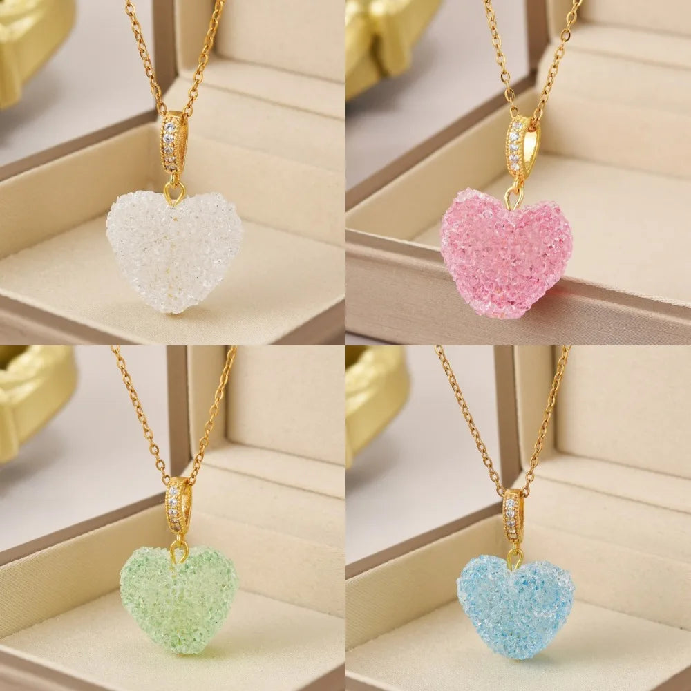 Four heart-shaped pendants in white, pink, green, and blue on gold chains against a beige background.