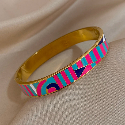 Gold bangle with colourful geometric pattern on a beige fabric background