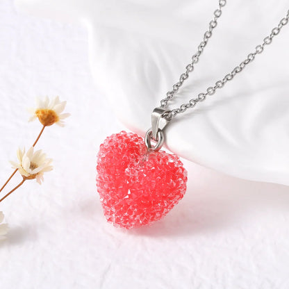 Red heart-shaped pendant on a silver chain with white flowers in the background