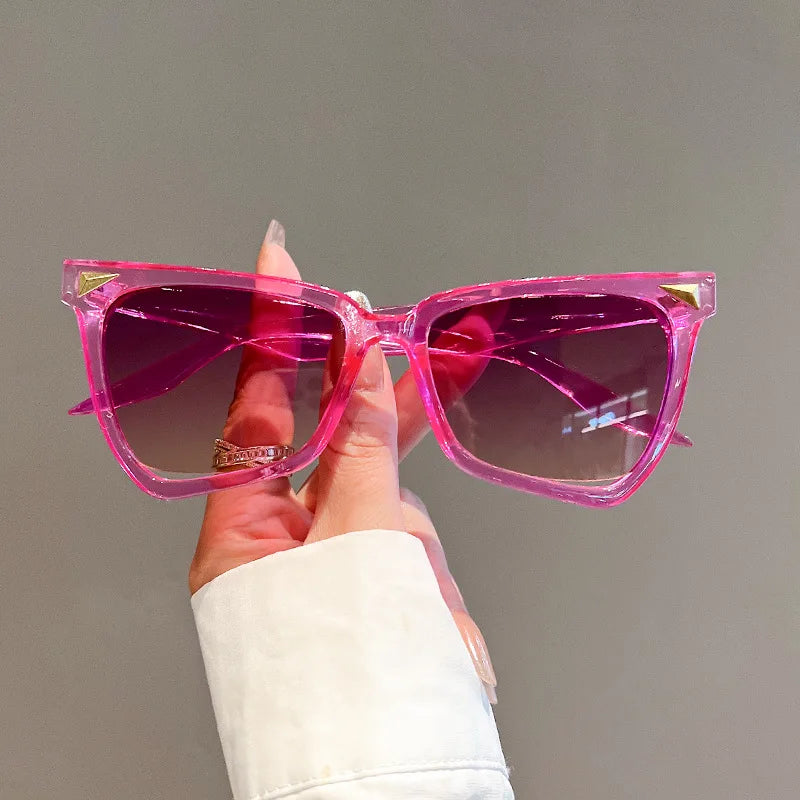 Pink sunglasses held by a hand against a neutral background