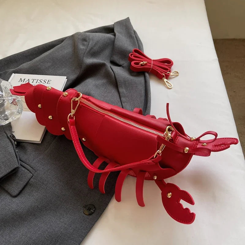 Red lobster-shaped handbag on a grey surface with a book and coat in the background.