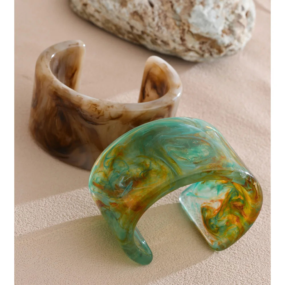Two unique bracelets on a beige surface with a rock in the background