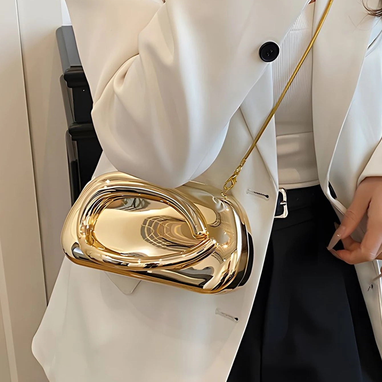 Gold handbag held by a person wearing a white coat.