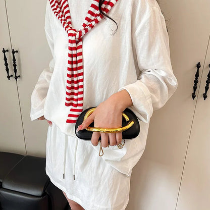 Person wearing a white outfit with a red and white striped scarf, holding a black clutch with gold handle.