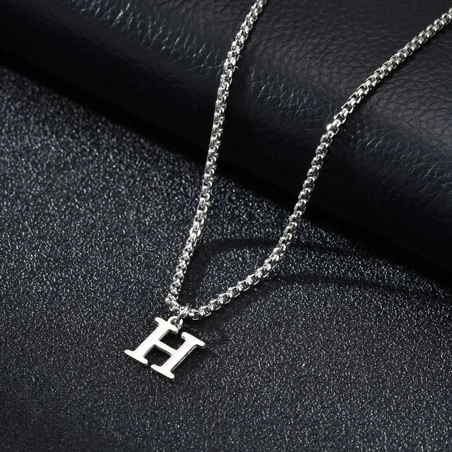 Silver necklace with a 'H' pendant on a black textured surface