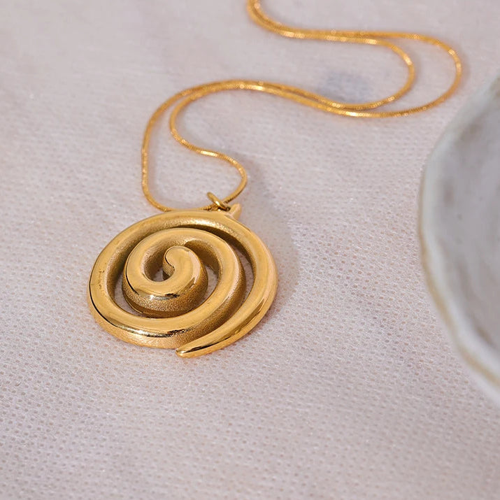 Gold spiral pendant necklace on a light fabric background