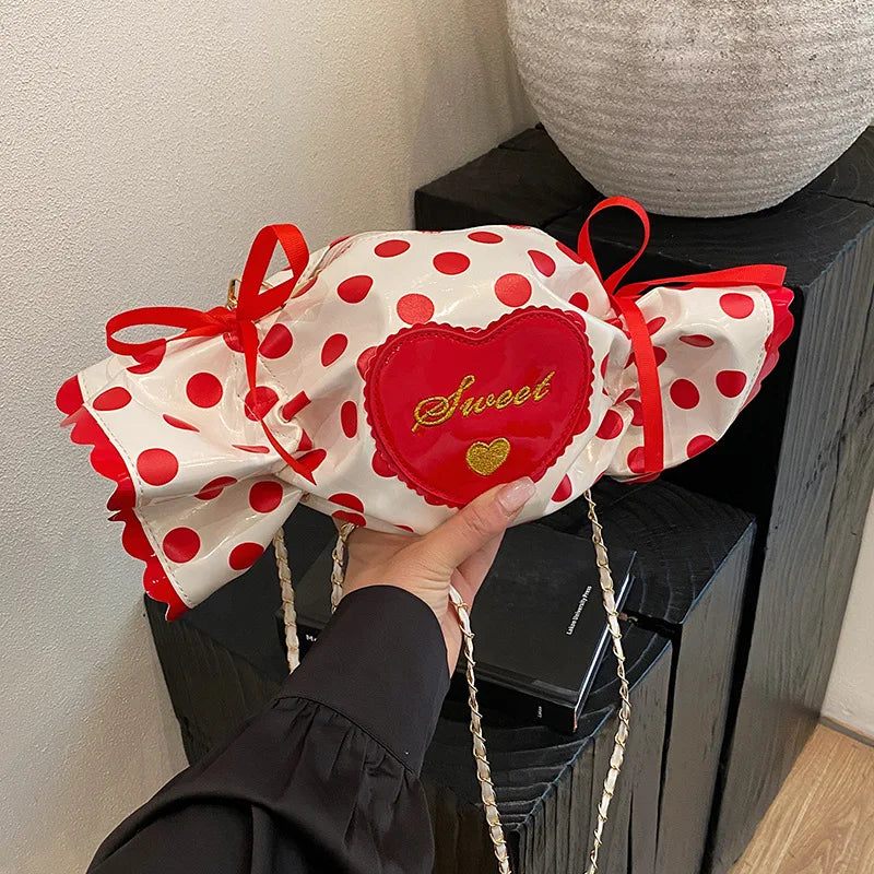 Red and white polka dot bra with 'sweet' heart design held by a hand against a neutral background.