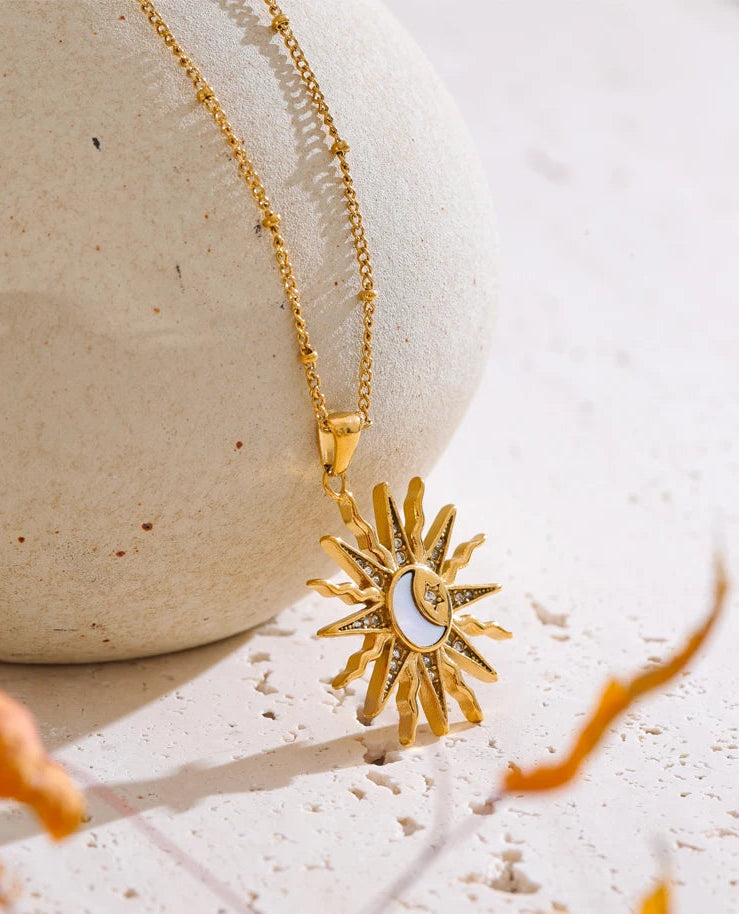 Gold necklace with a sun and moon pendant on a textured surface