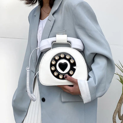 Person holding a white handbag designed like an old-fashioned telephone with a heart symbol.