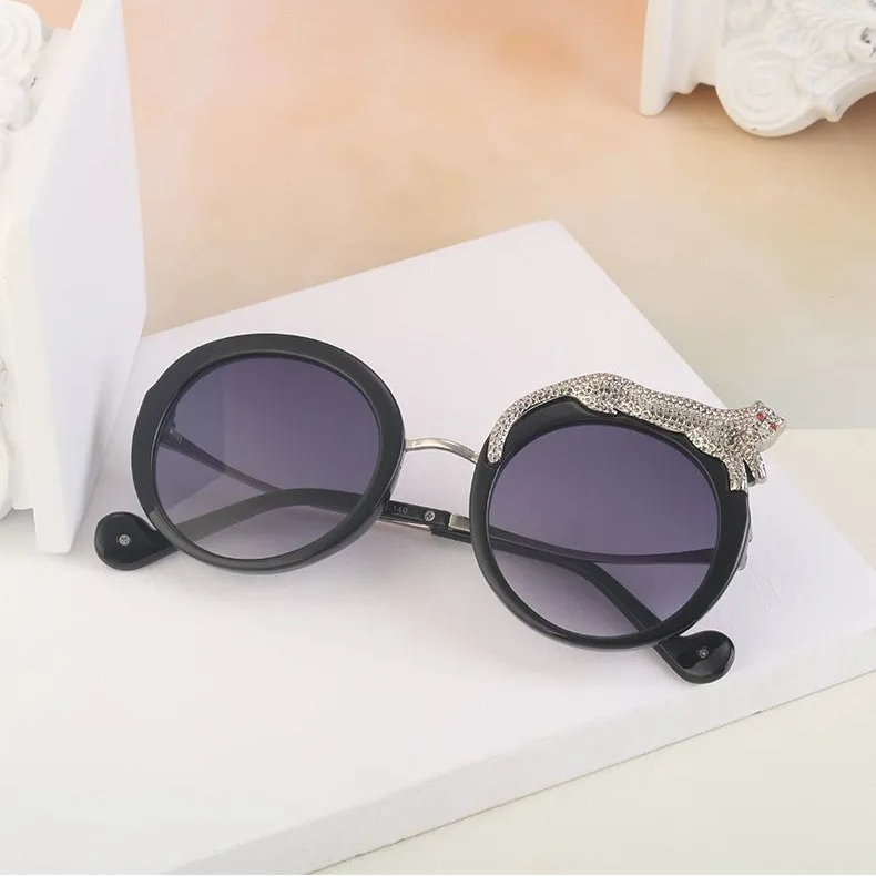 Round sunglasses with black frames and dark lenses on a white surface.
