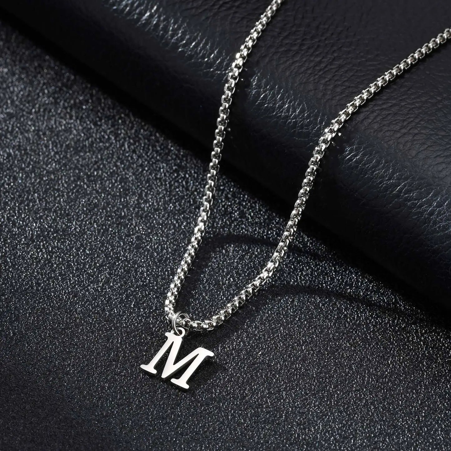 Silver necklace with a 'M' pendant on a black textured surface