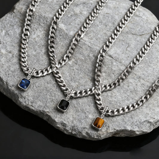 Three silver chain necklaces with pendant stones on a stone surface