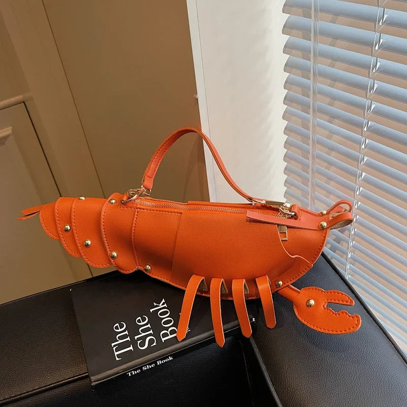 Orange lobster-shaped handbag on a surface with a book titled 'The She Book' in the background.