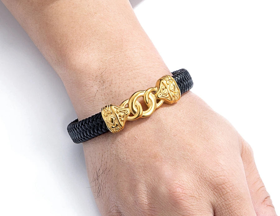Gold bracelet with a black cord on a wrist against a white background