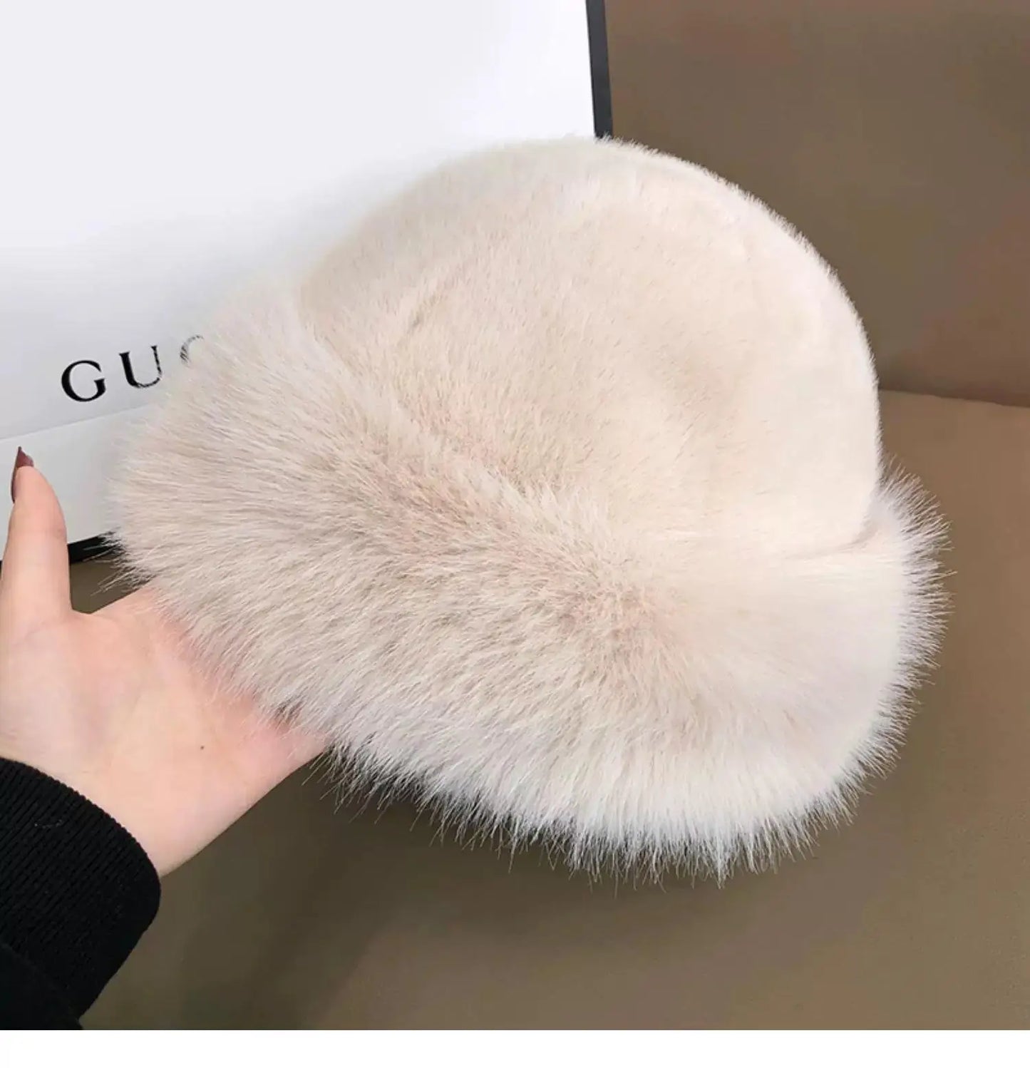 White fluffy hat held by a hand with a Gucci box in the background