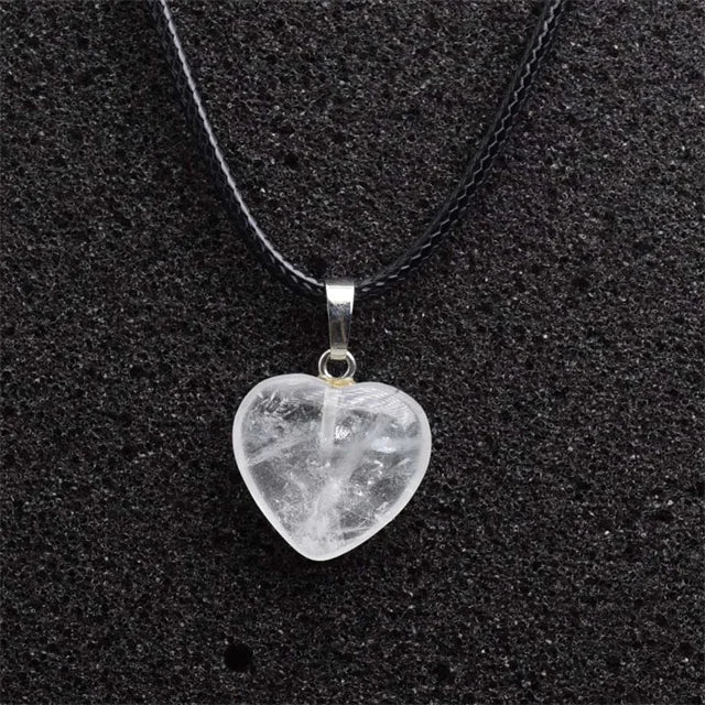 Heart-shaped crystal pendant on a black cord against a black background