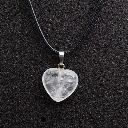 Heart-shaped crystal pendant on a black cord against a black background