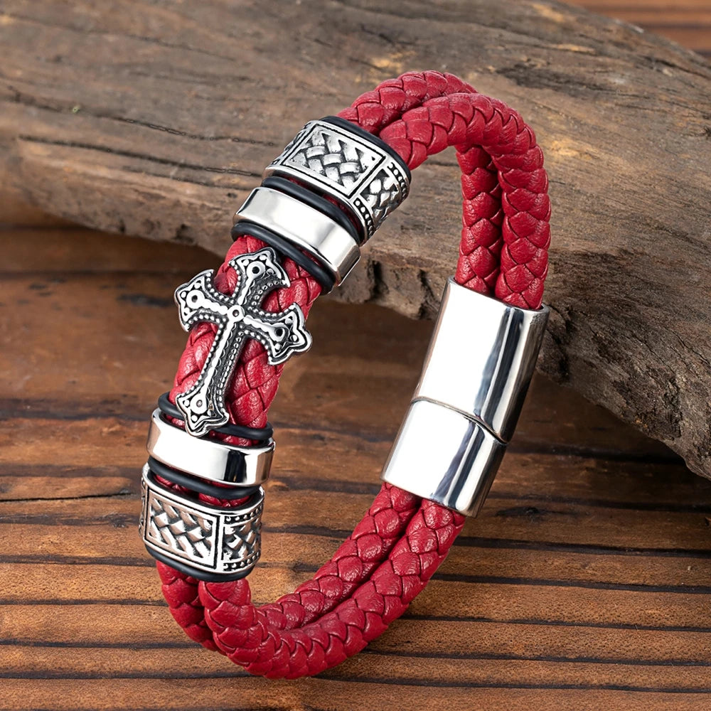 A red braided leather bracelet with silver-toned metal accents, including a cross charm and textured spacer beads, displayed on a rustic wooden surface.