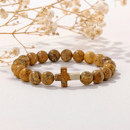 Beaded bracelet with a cross charm on a light background with dried flowers.