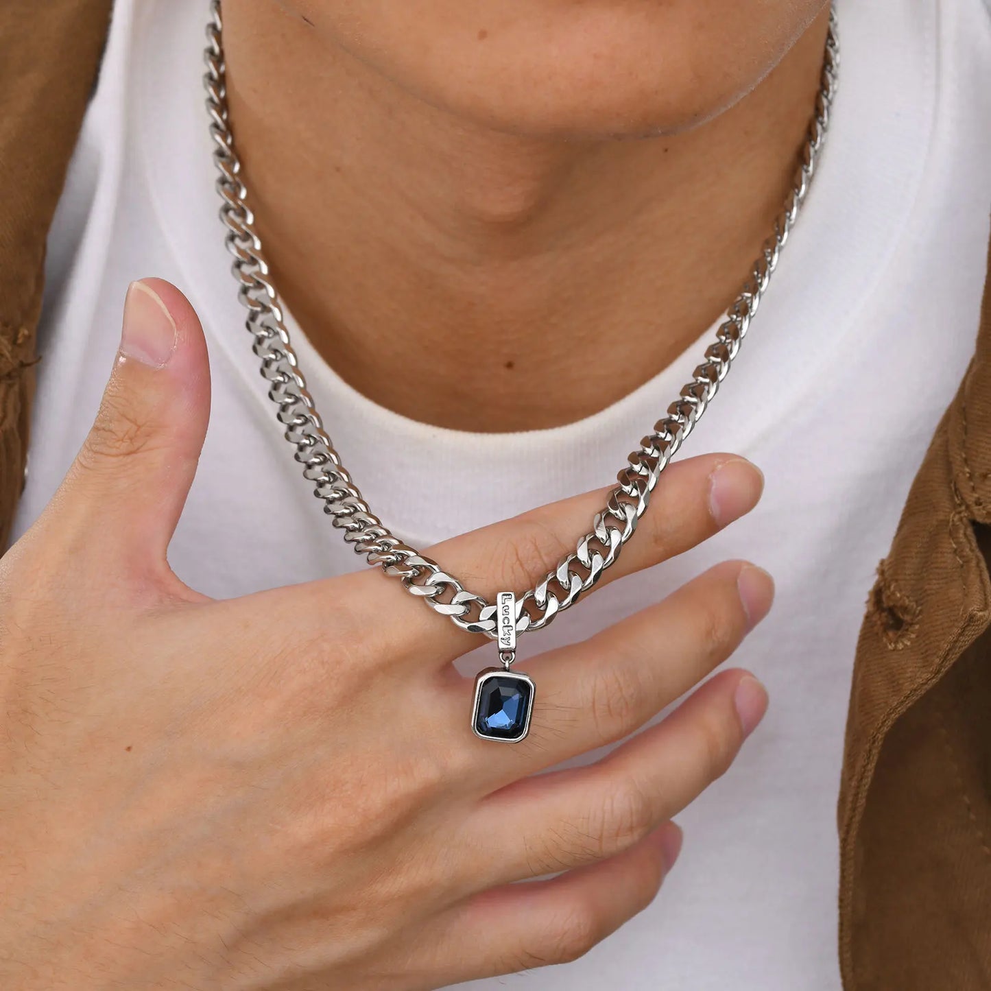 Person wearing a silver chain necklace with a blue pendant, holding it with their hand.
