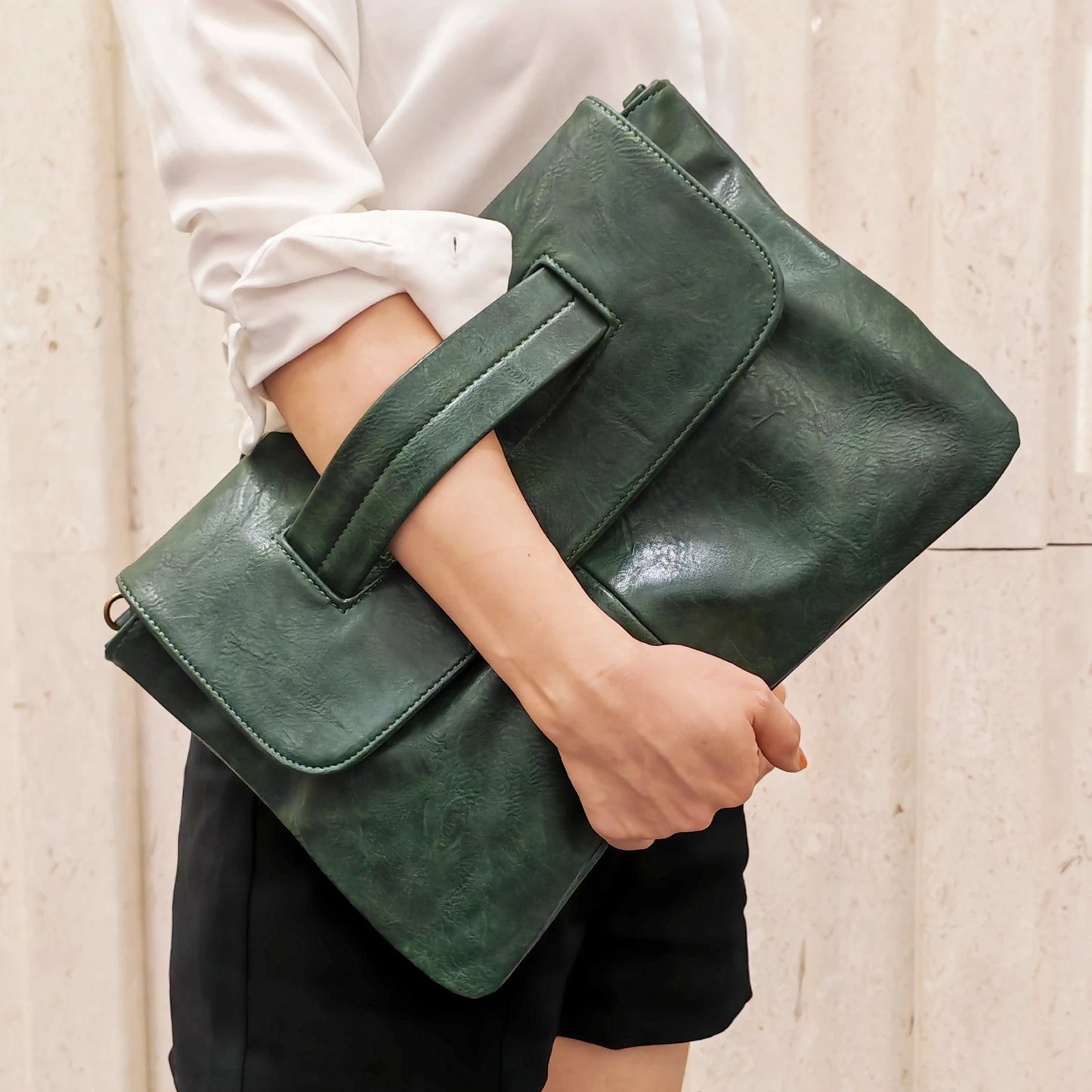 Green leather clutch held by a person against a neutral background