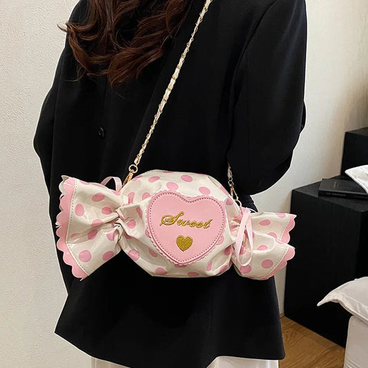 Person holding a pink polka dot candy-shaped bag with 'Sweet' text in a room.