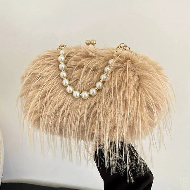 Beige feathered handbag with pearl chain held by a hand against a white background