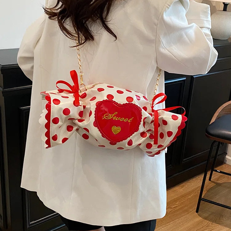 Person wearing a white coat holding a red and white polka dot candy-shaped bag.