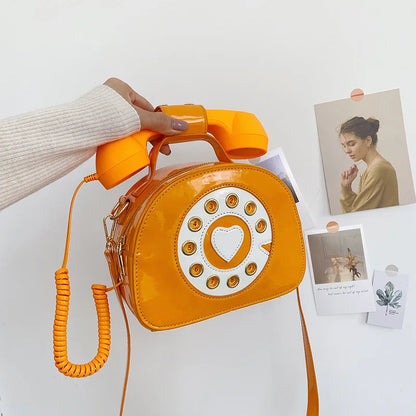 Yellow rotary phone-shaped handbag held by a person on a white background