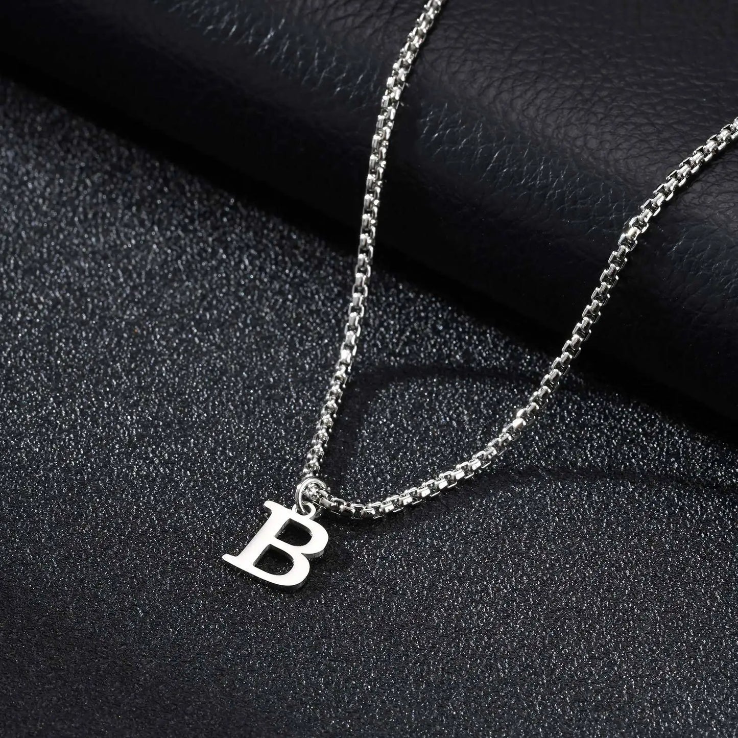 Silver necklace with a 'B' pendant on a black textured surface