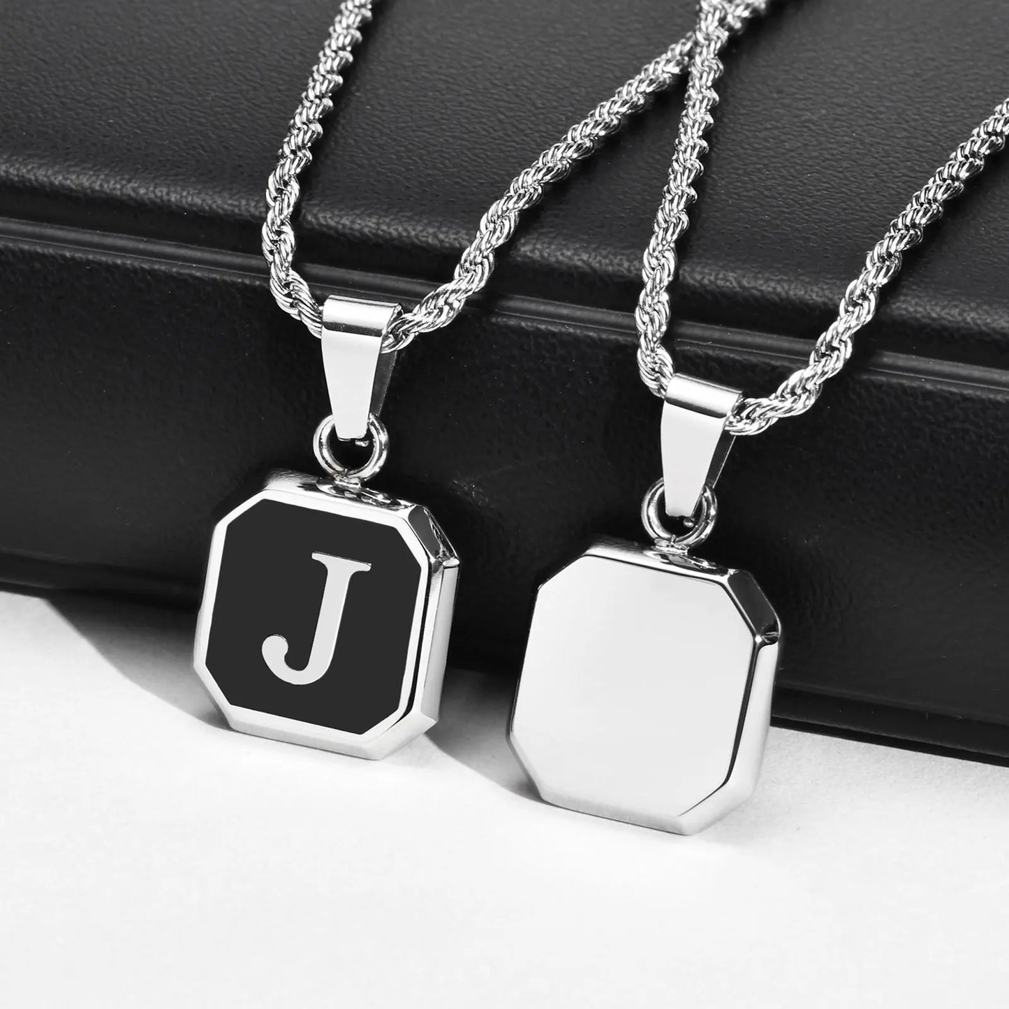 Two silver necklaces with hexagonal pendants on a black surface
