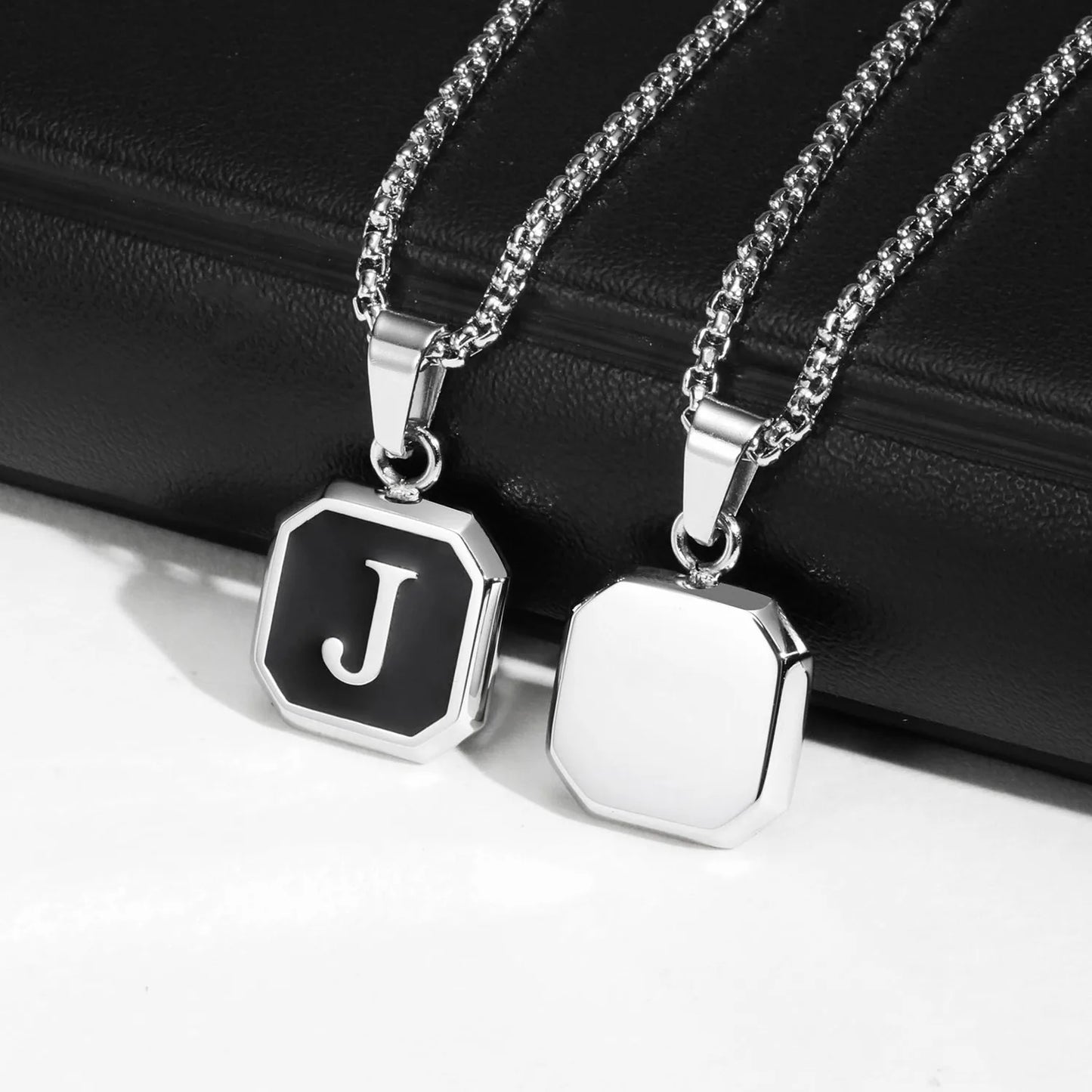 Two silver necklaces with hexagonal pendants on a black surface