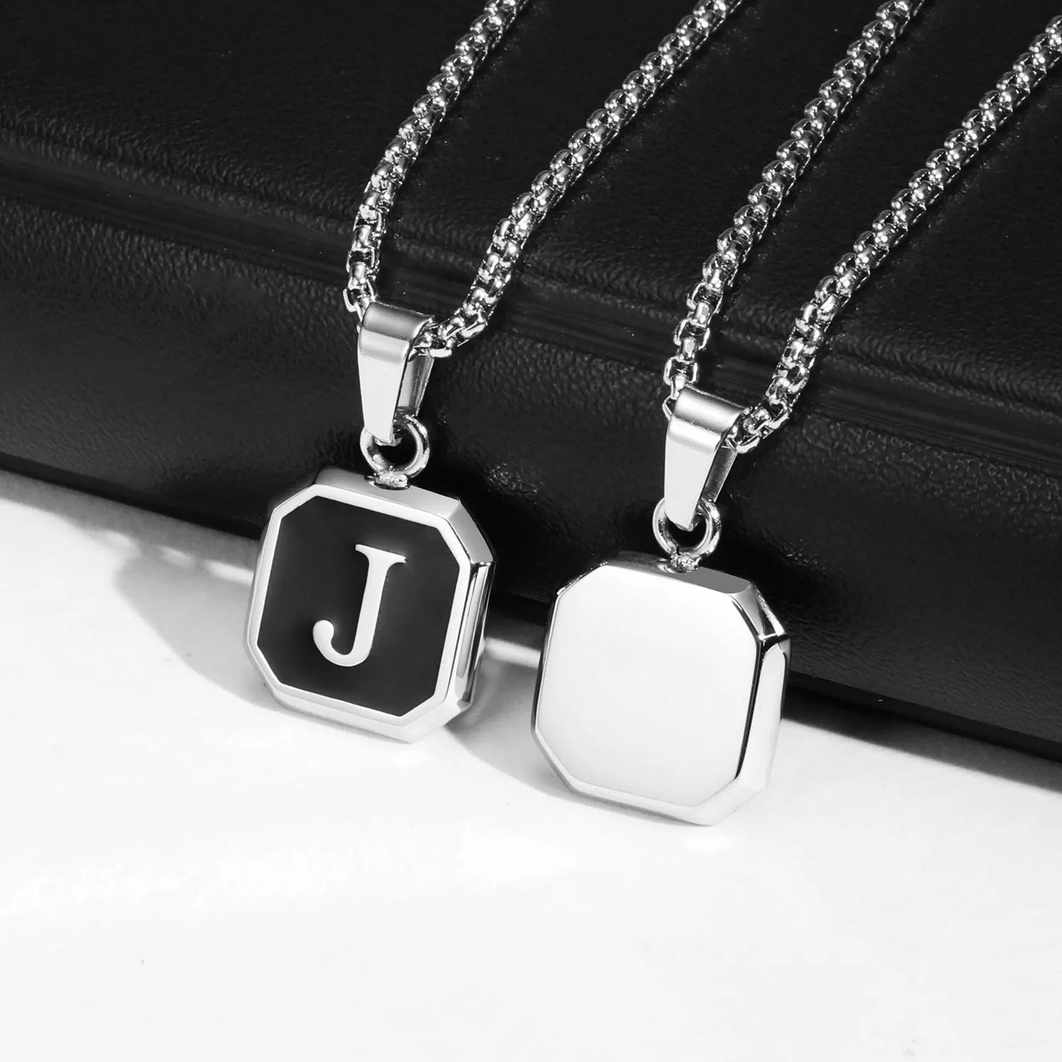 Two silver necklaces with hexagonal pendants on a black surface