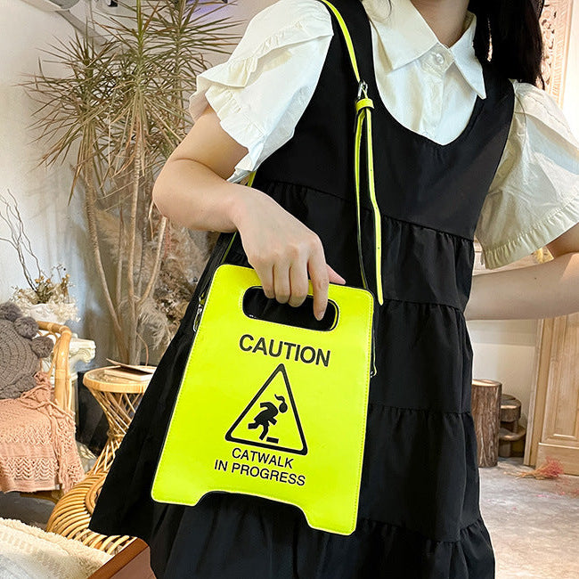 Person holding a bright yellow 'Caution: Catwalk in Progress' sign in an indoor setting.