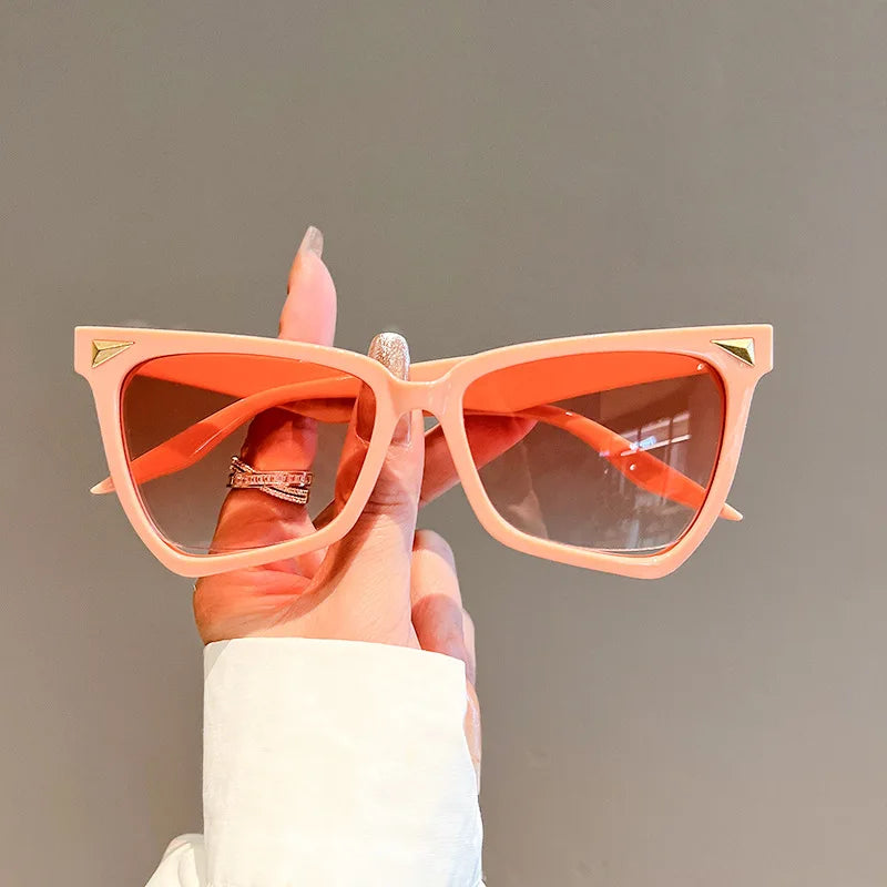 Hand holding peach-coloured sunglasses with a plain background