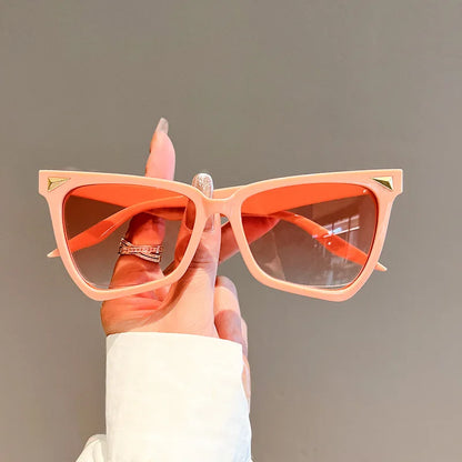 Hand holding peach-coloured sunglasses with a plain background