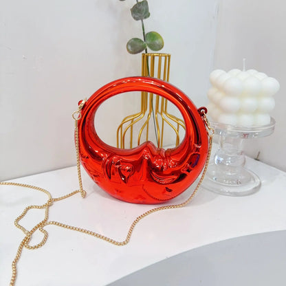 Red crescent handbag with gold chain on a white surface with decorative items.